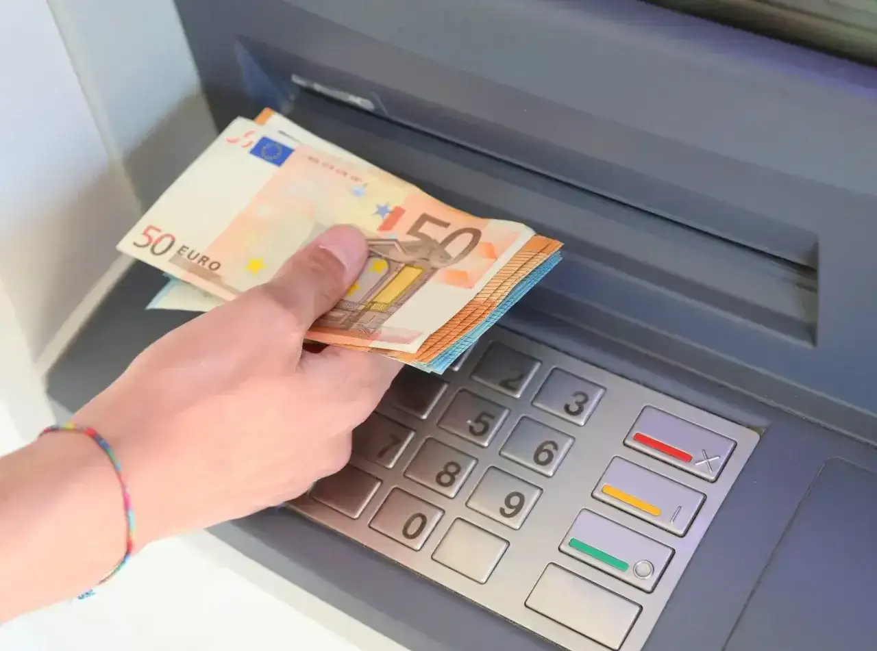 Ręka trzyma banknoty 50 euro, waluta Hiszpanii, przy bankomacie.