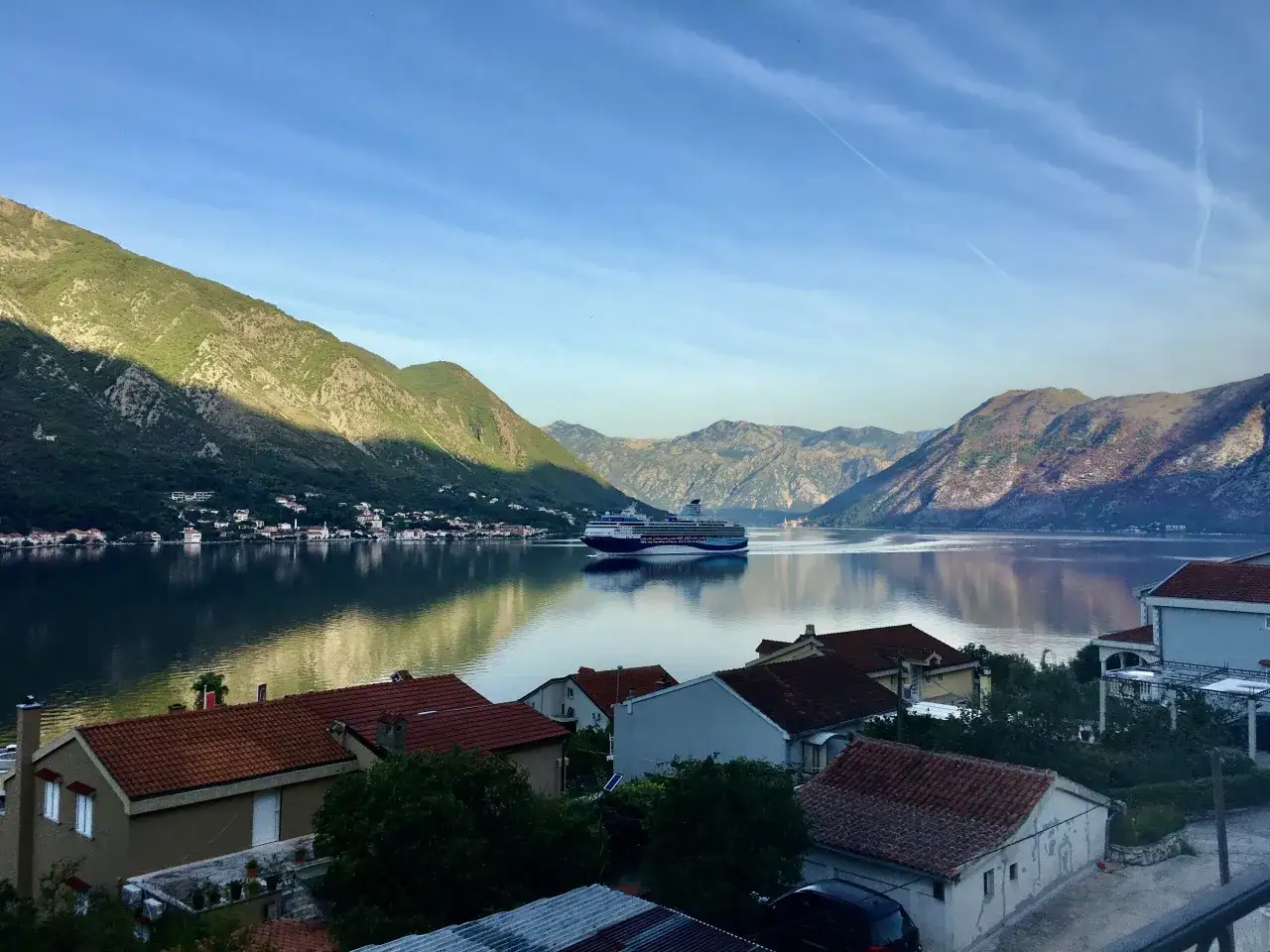 Widok na zatokę z górami w tle, statkiem wycieczkowym i domami. Czy czarnogóra jest bezpieczna? Tak, to spokojne miejsce.