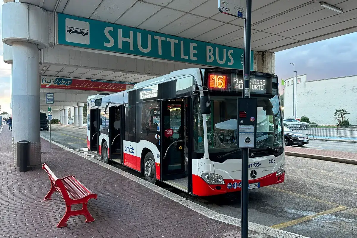 Autobus wahadłowy na lotnisko, z numerem 16, gotowy do odjazdu. Czerwona ławka czeka na pasażerów.