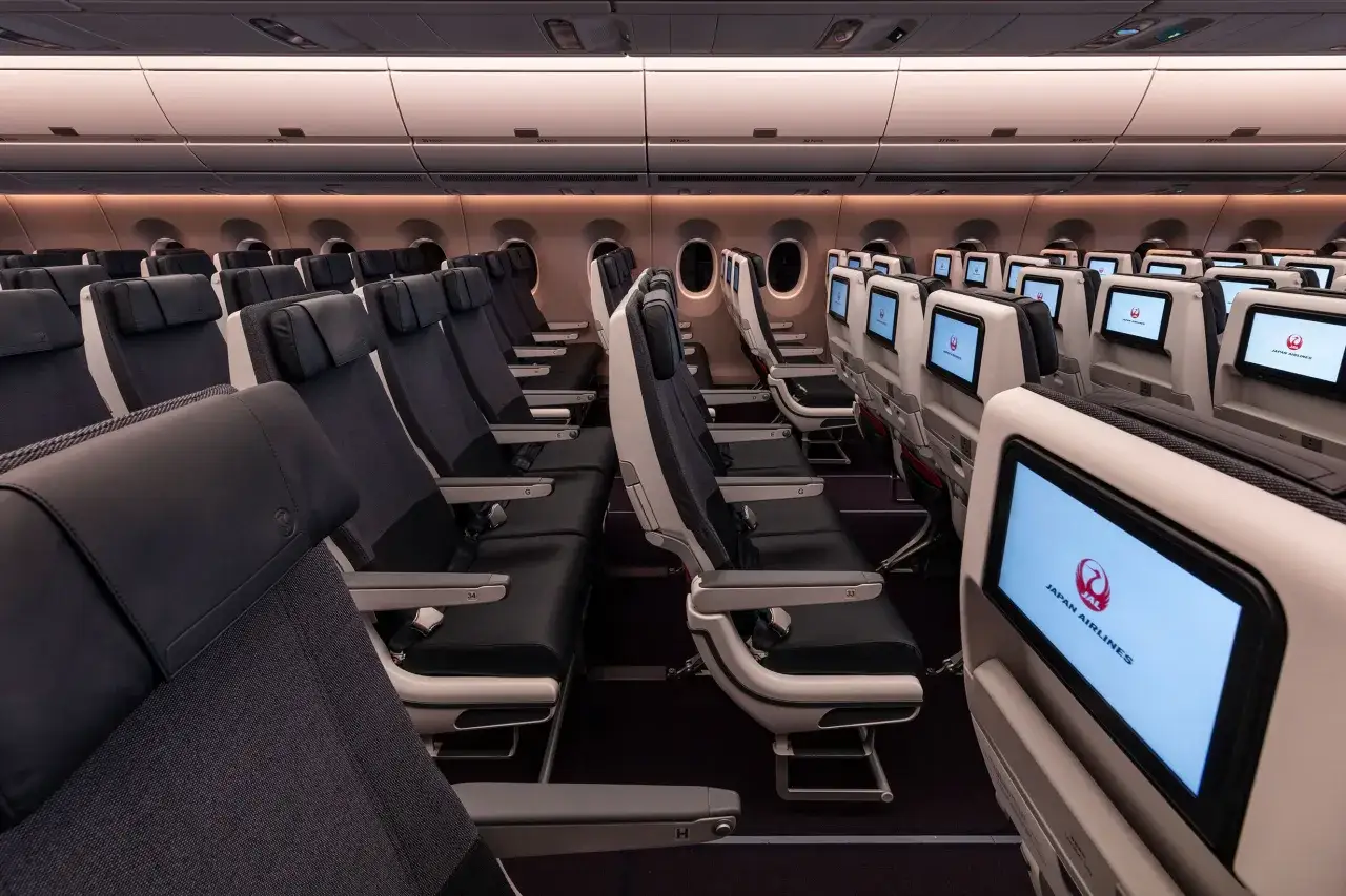 Wnętrze samolotu Airbus A350-900 linii Japan Airlines. Rzędy ciemnych foteli z ekranami pokładowymi.