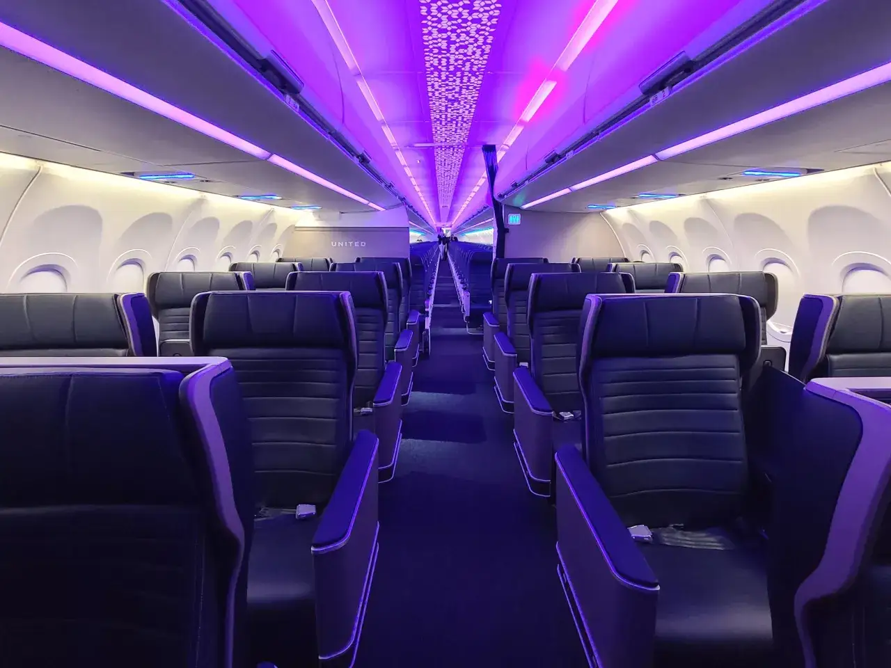 Wnętrze samolotu Airbus A321neo linii United, oświetlone fioletowym blaskiem, z rzędami ciemnych, wygodnych foteli.