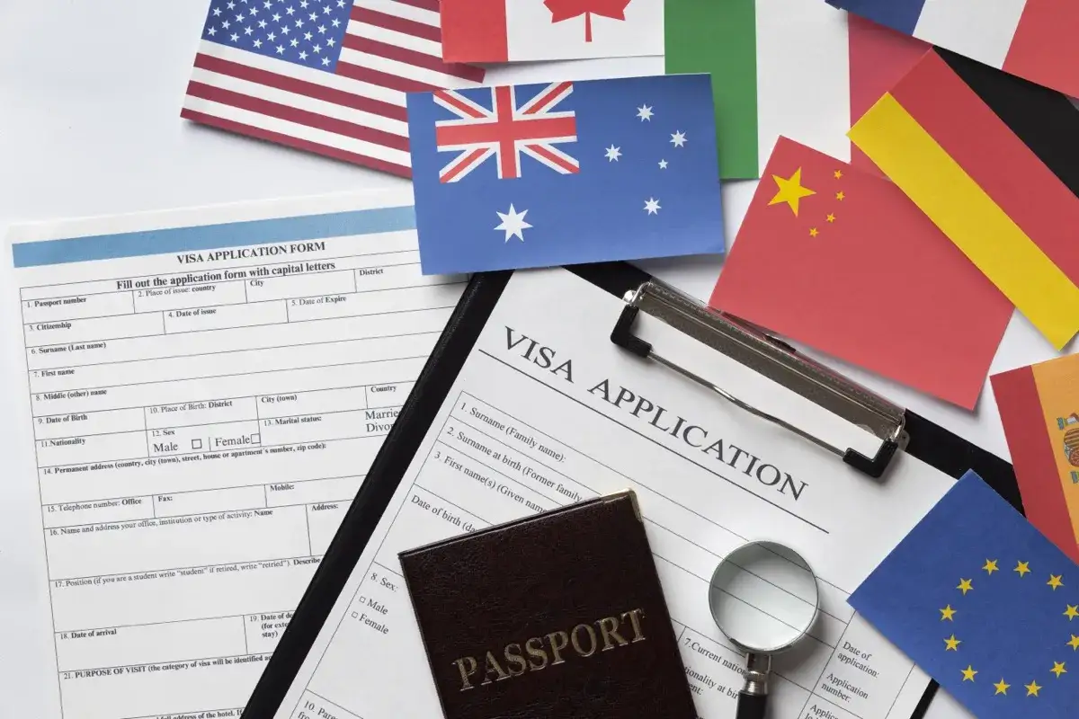 Formularze wizowe, paszport i flagi różnych krajów, w tym Australii, sugerują przygotowania do podróży. Planujesz wyjazd do Nowej Zelandii? Wiza to pierwszy krok.