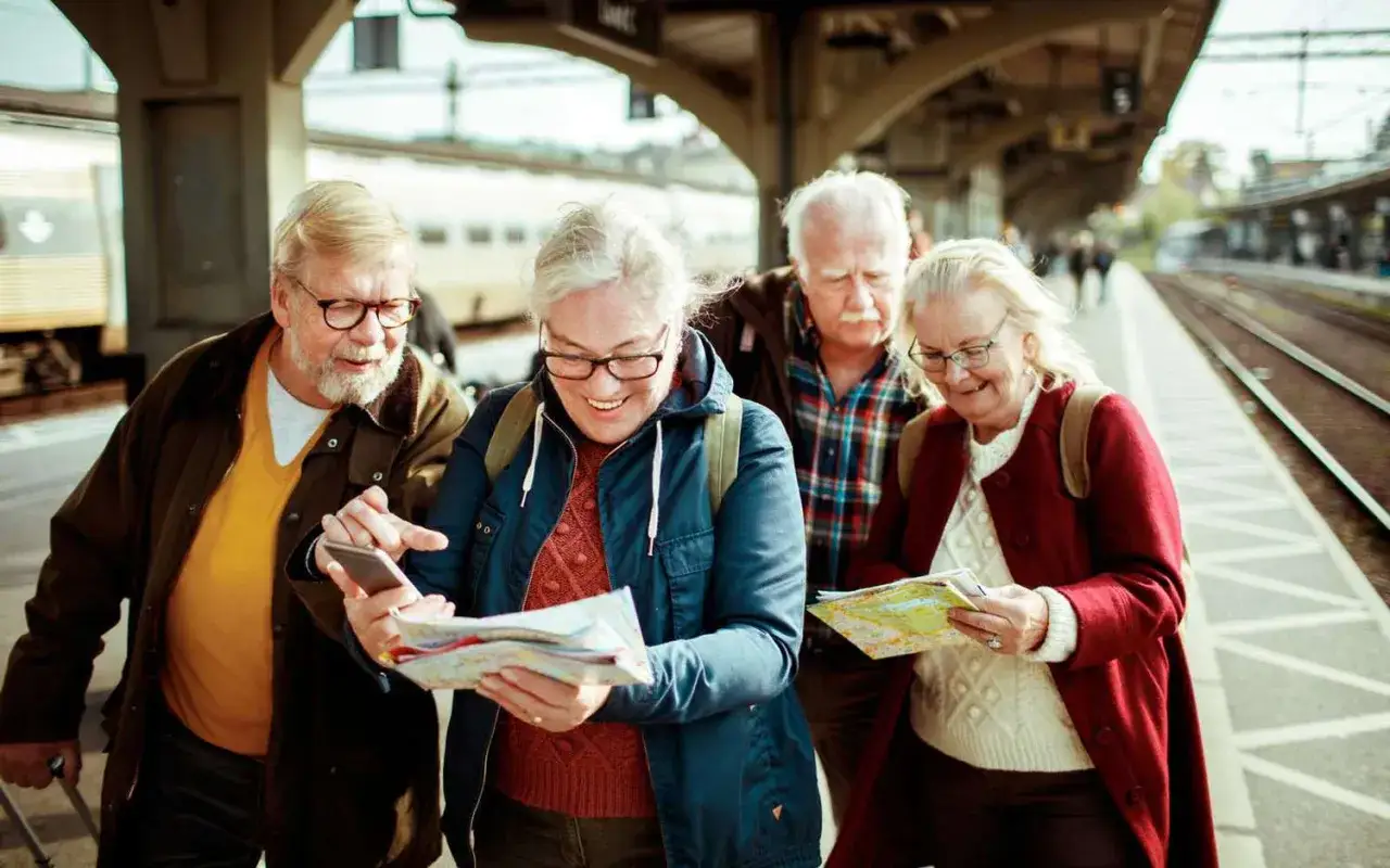 Grupa seniorów planuje wczasy dla emerytów z dojazdem, studiując mapę na dworcu kolejowym.