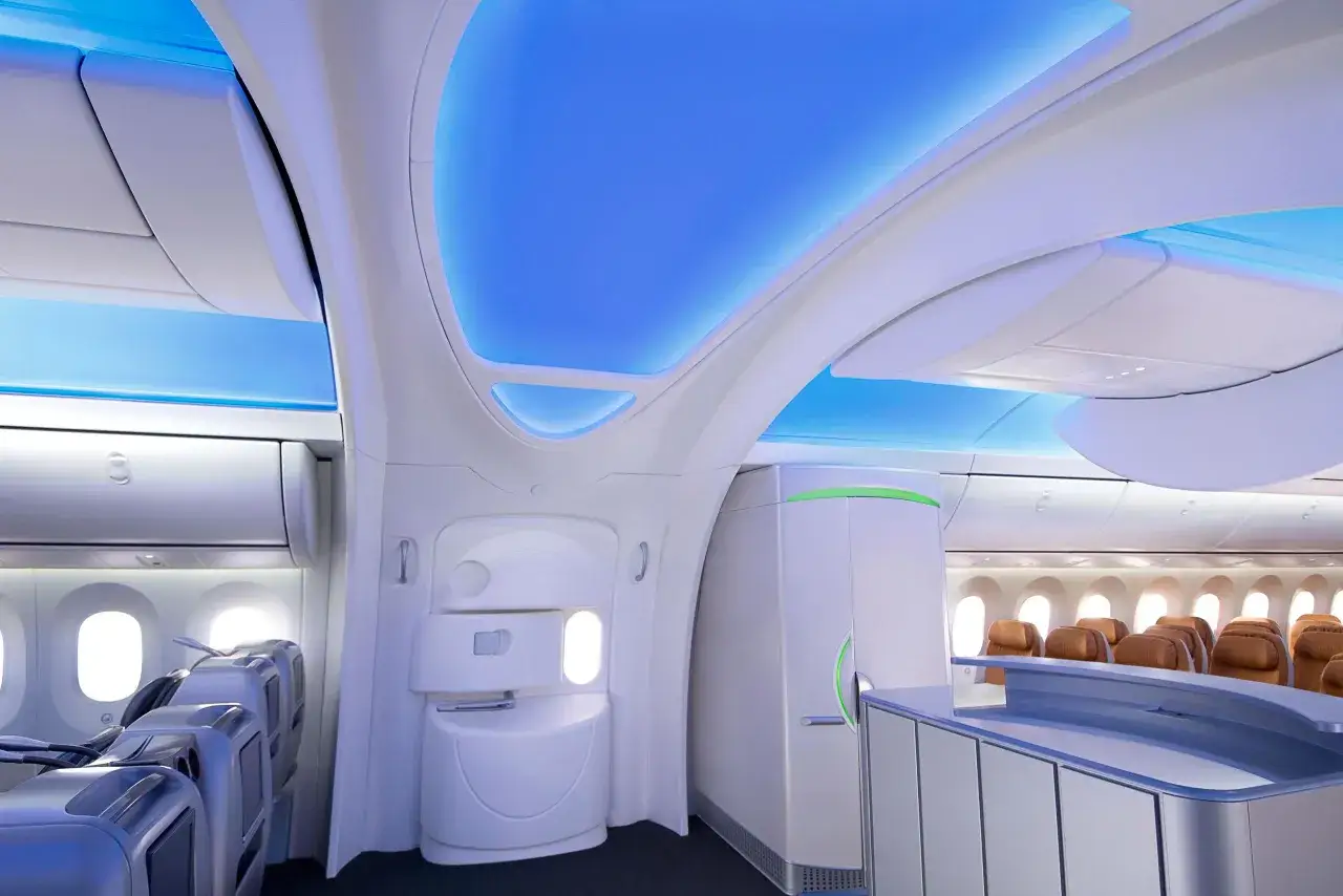 Nowoczesne wnętrze samolotu 787 Dreamliner z niebieskim podświetleniem sufitu i brązowymi fotelami.