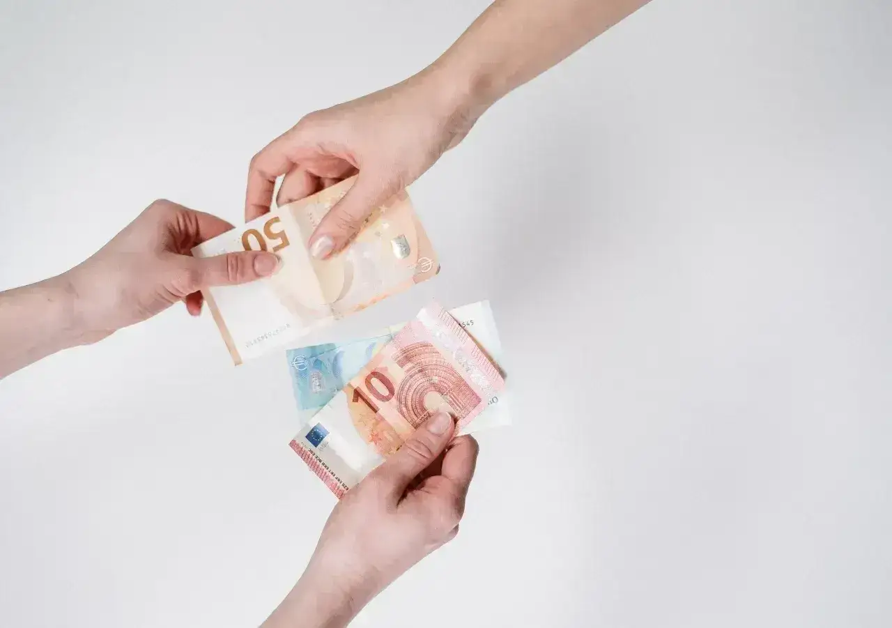 Dwie ręce przekazują sobie banknoty euro. W Holandii obowiązuje euro, więc to typowy widok przy płatnościach.