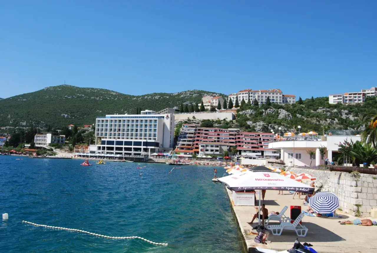 Hotel Sunce Neum w Neum, Bośnia i Hercegowina, z widokiem na turkusowe morze i zielone wzgórza. Słoneczny dzień na plaży.
