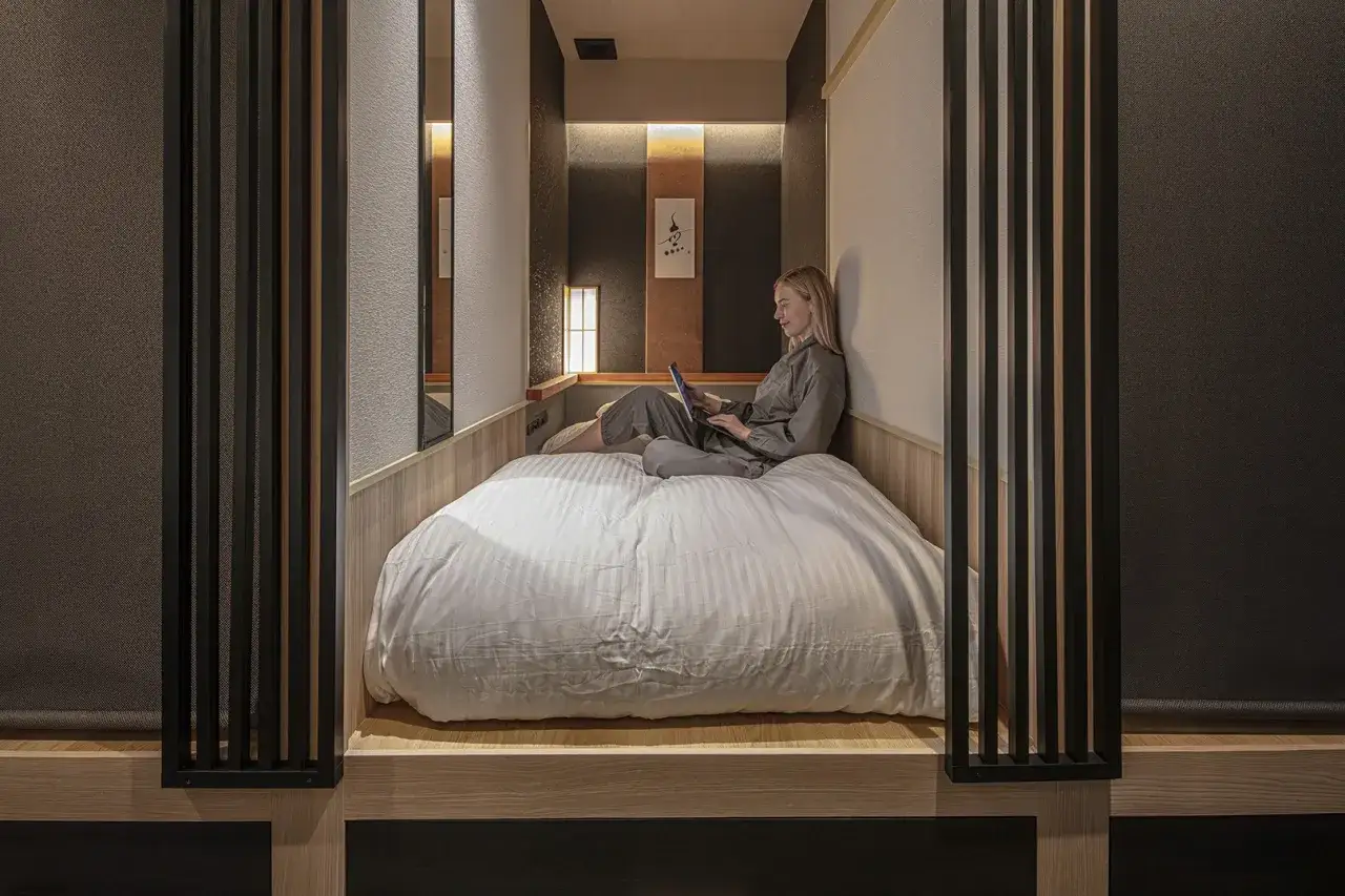 Kobieta relaksuje się w przytulnym hotelu kapsułowym, korzystając z laptopa na wygodnym łóżku.